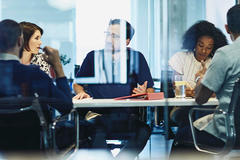 view through glass of 5 people sitting at a conference table working